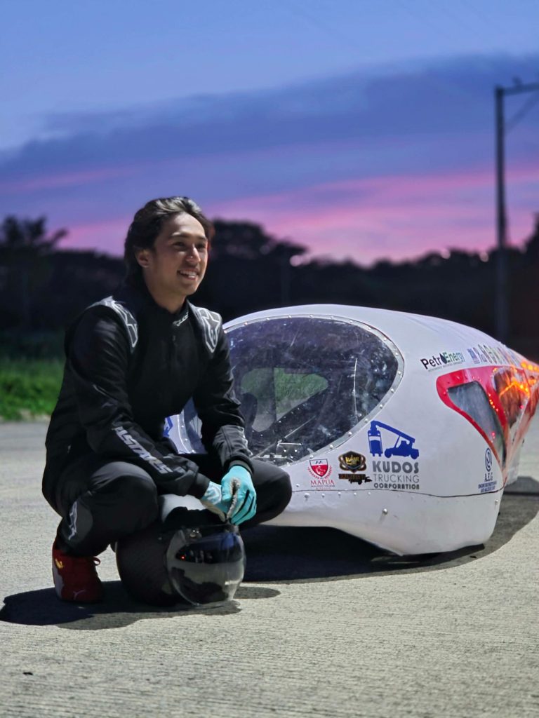 Driver of the Mapúa Mindanao Shell Eco-Marathon team kneels beside the team’s energy-efficient vehicle.