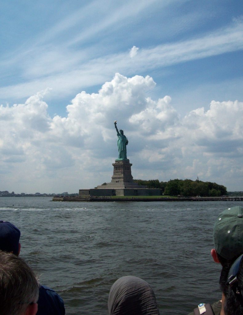 The Statue of Liberty seen from a distance across New York Harbor on a bright day.