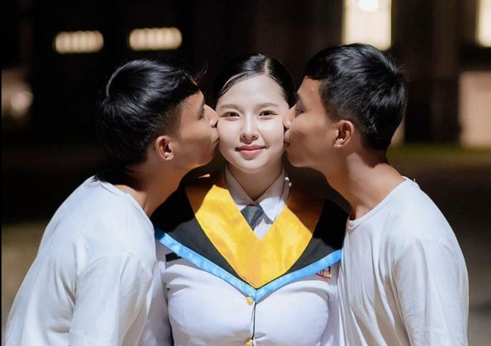 A Thai woman stands between twin brothers during a public event, part of a Thai woman twin brothers relationship that has drawn online attention.