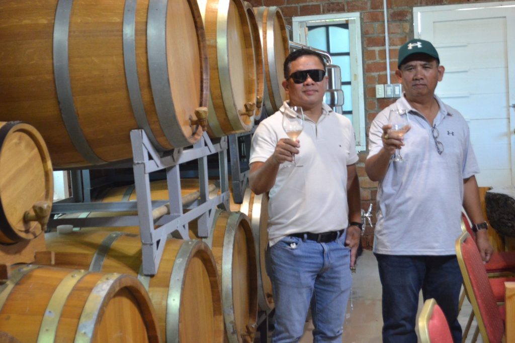 Men holding wine glasses beside wooden barrels made from Davao-grown grapes